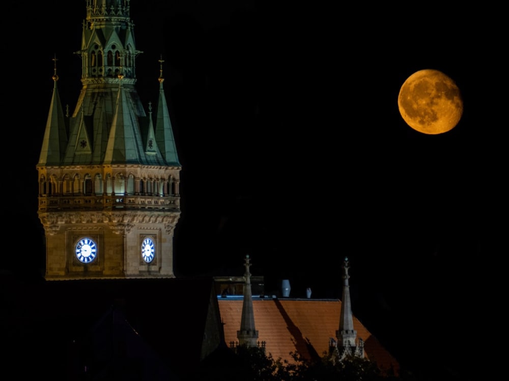 The moon rises at night next to the tower of the old town hall