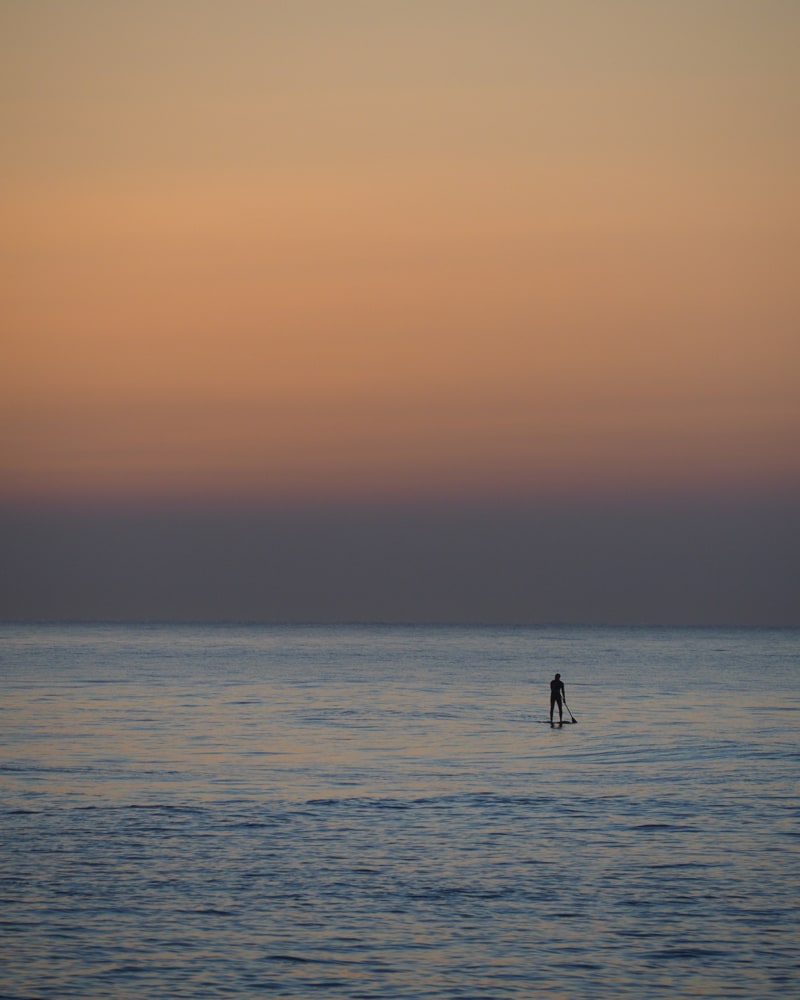 A stand-up paddler on the sea uses the first light at sunrise