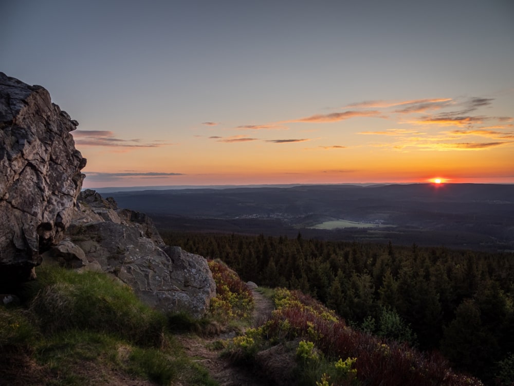 The setting sun illuminates stones of the Wolfsscharte in the foreground as it goes down behind a mountain range.