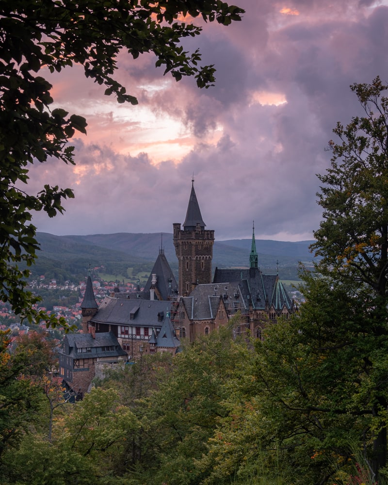 The castle of Wernigerode at sunset situated against dark and purple, orange clouds in the background.