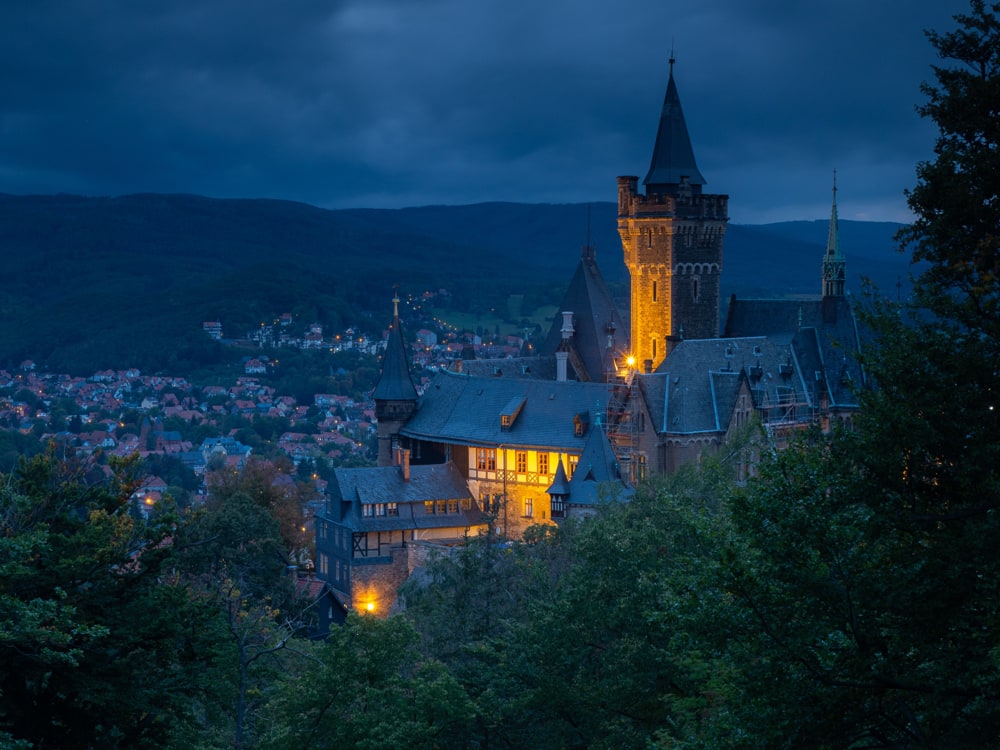 The castle of Wernigerode at blue hour overlooks the city lights of some residential streets in Wernigerode.