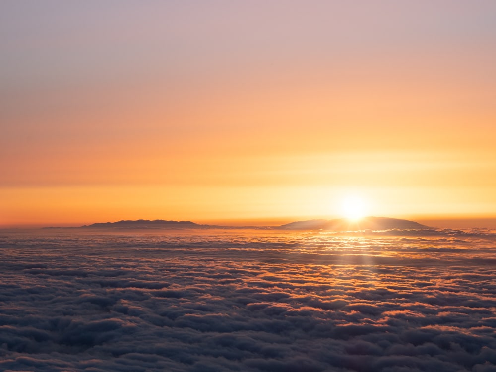 A sun star is formed by the setting sun over La Palma. The walls around the Caldera de Taburiente and the ridge of the Cumbre Vieja is seen above orange clouds over the Atlantic Ocean.